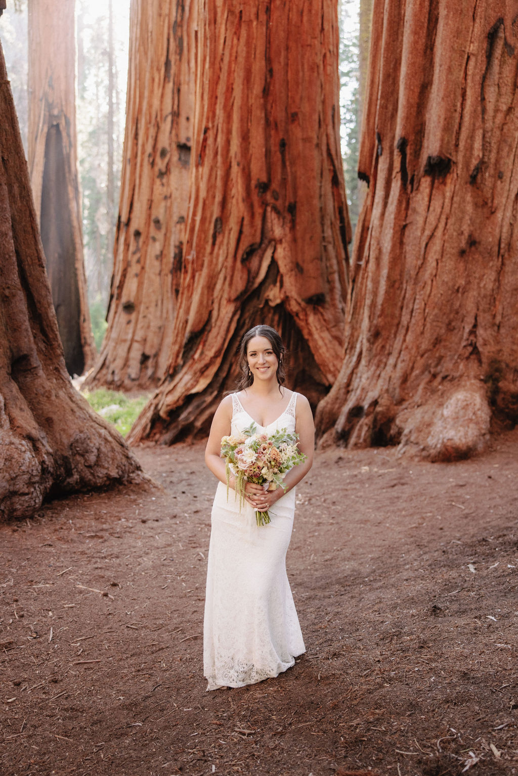 A bride in a white gown holds a bouquet while standing in front of large redwood trees 
Top 5 reasons to elope in sequoia national park