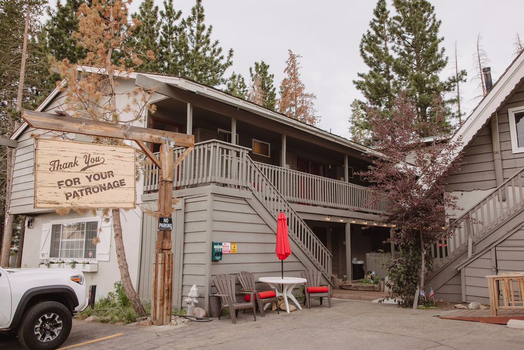 A two-story wooden building with a triangular roof and brown exterior. An American flag and a California state flag hang beside the entrance, with a small sign near the peak of the roof