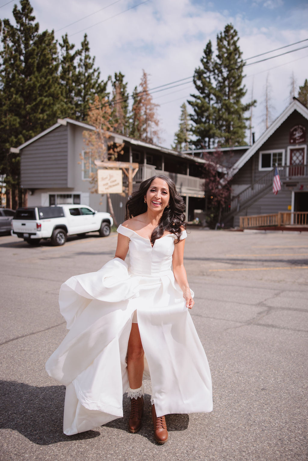 A woman in a white dress is getting into a white SUV with the rear door open in an outdoor setting. Trees and part of a building are visible in the background.