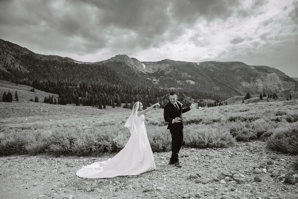 A bride in a white dress and groom in a suit stand in a vast, open field with mountains in the background, under a cloudy sky at mammoth lakes