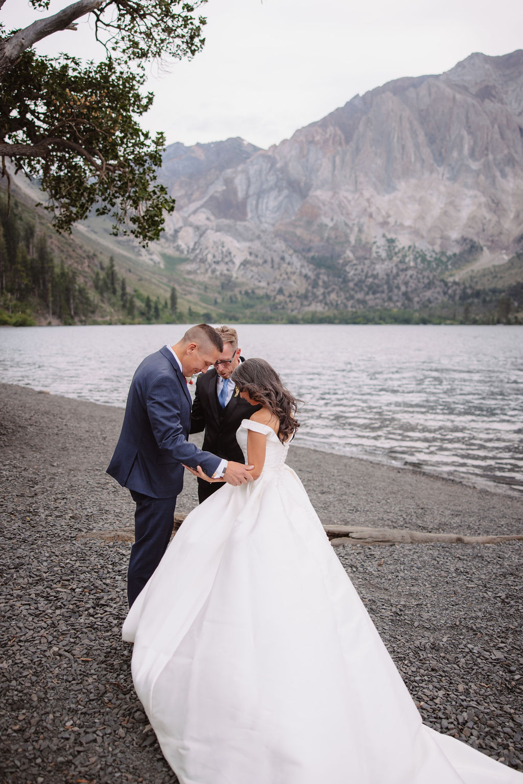 A wedding ceremony by a lakeside, with a couple in formal attire and a man officiating for a mammoth lakes elopement