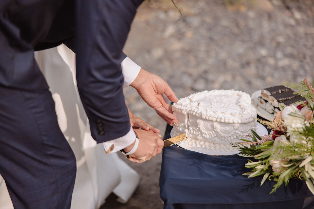 A heart-shaped white cake with the words "Just Married" inscribed on it, surrounded by piped icing. A cake server and knife are placed beside the cake on a dark tablecloth.