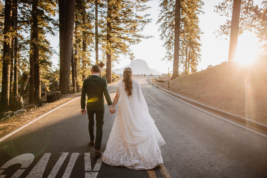 A couple in wedding attire stand together on a rocky overlook with a mountain landscape in the background at Yosemite national park at glacier point and mariposa grove 