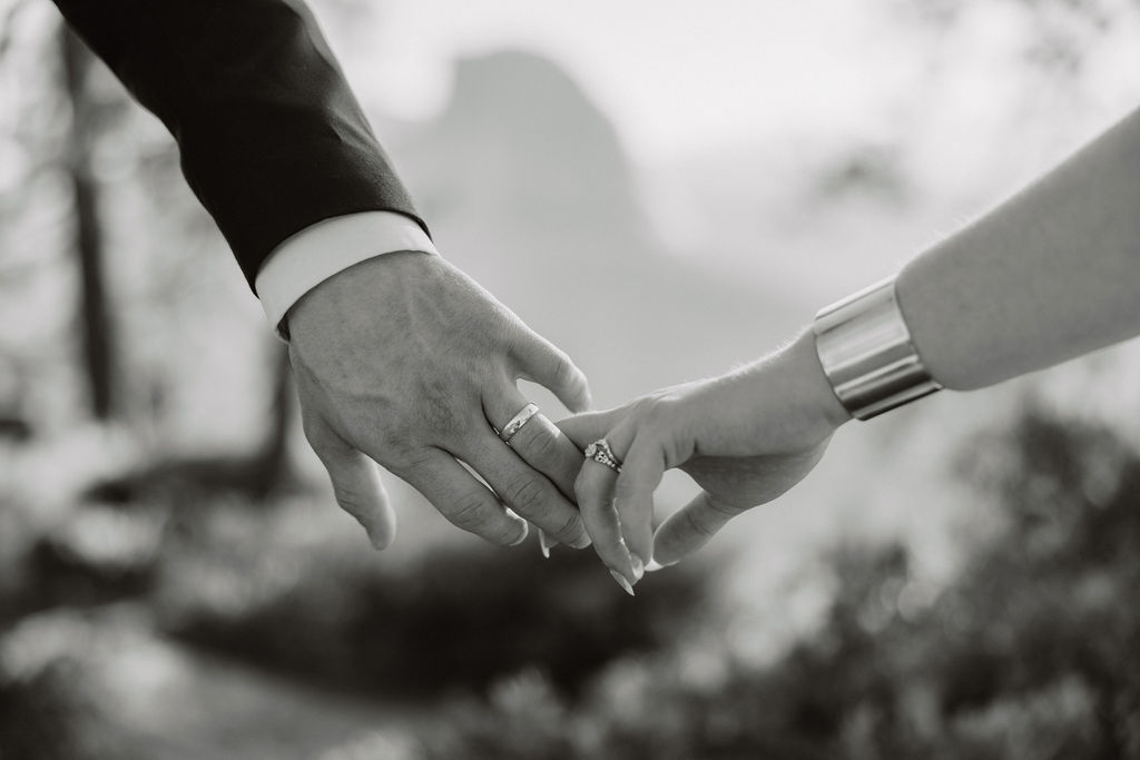 A black and white photo of two hands reaching out to each other, with one wearing a metallic bracelet.