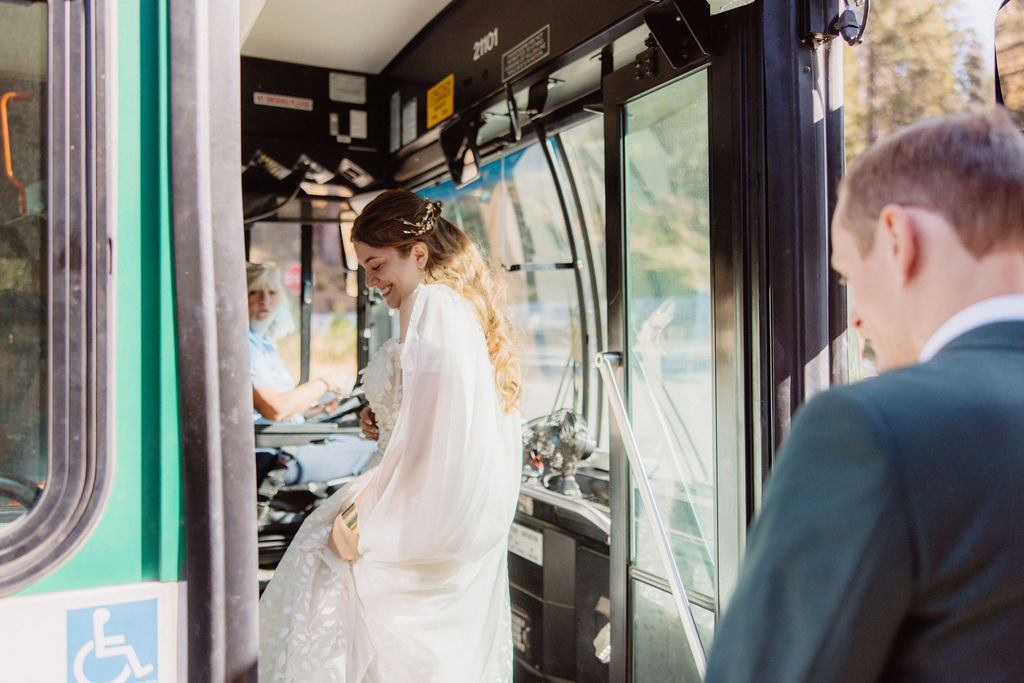 A bride in a white dress steps onto a bus, followed by a man in a suit.