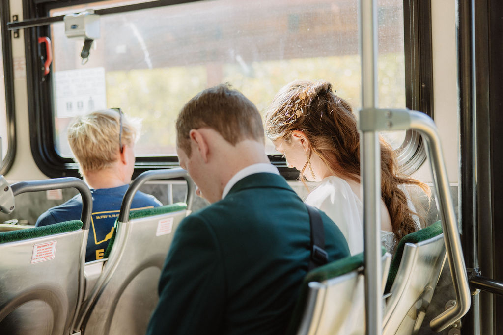 A bride in a white dress steps onto a bus, followed by a man in a suit.