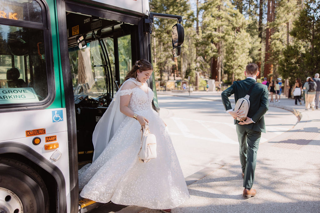 A bride in a white dress steps onto a bus, followed by a man in a suit.