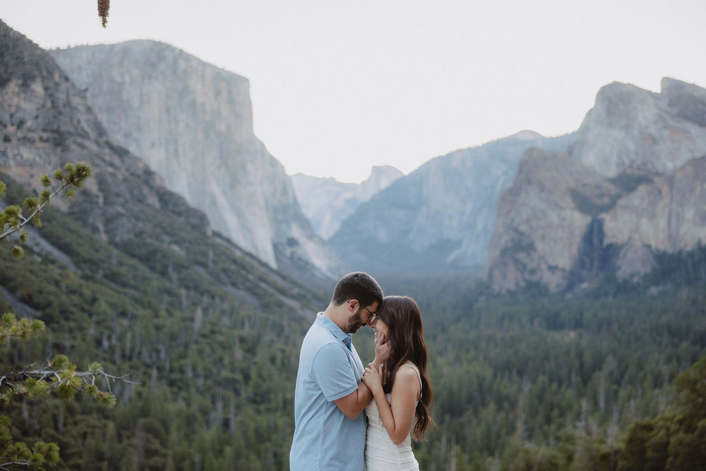 A couple stands closely together in an embrace with a mountainous landscape in the background.