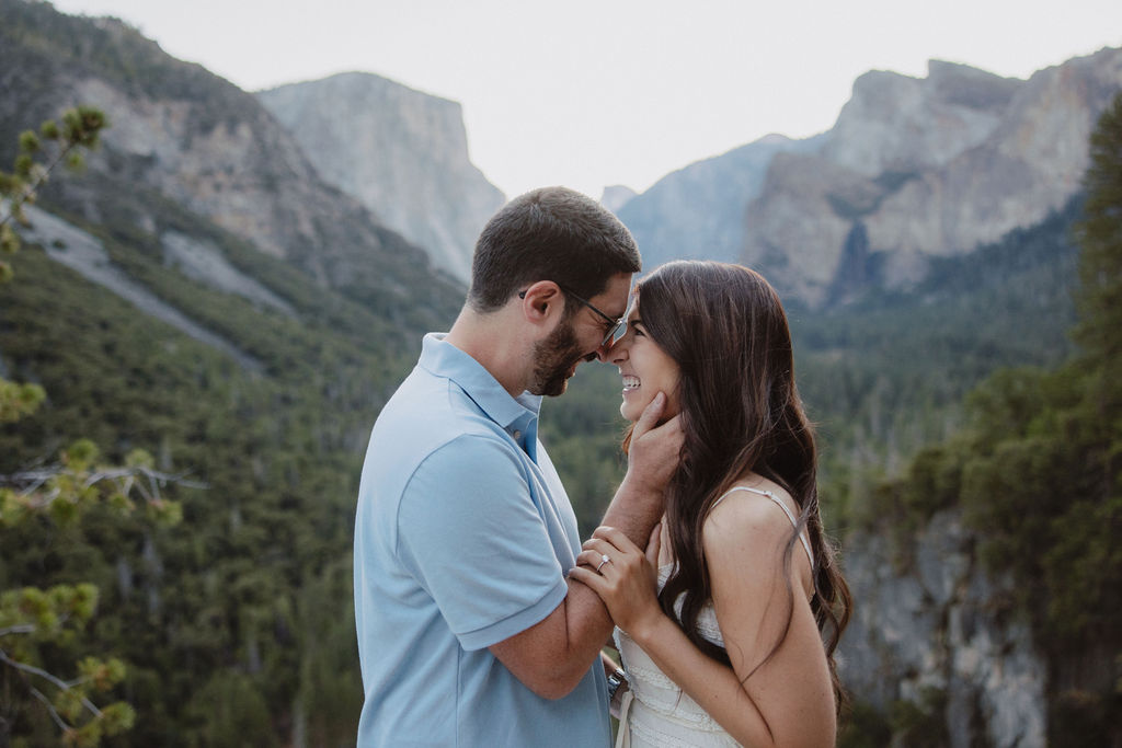 A couple smiling at each other in a mountainous landscape, with trees and cliffs in the background Yosemite National Park Engagement Photos 