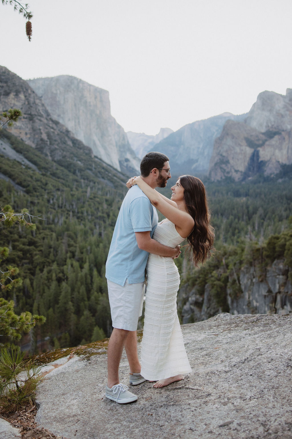 A couple smiling at each other in a mountainous landscape, with trees and cliffs in the background Yosemite National Park Engagement Photos 