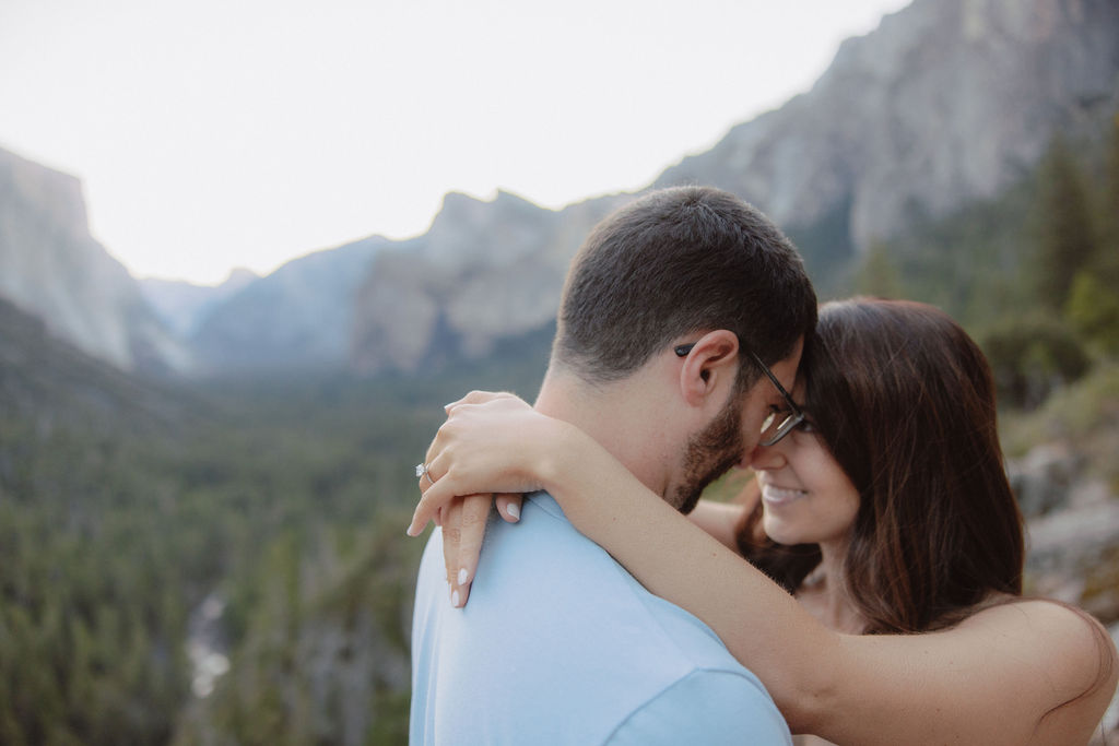 A couple embraces with a scenic mountain landscape in the background.