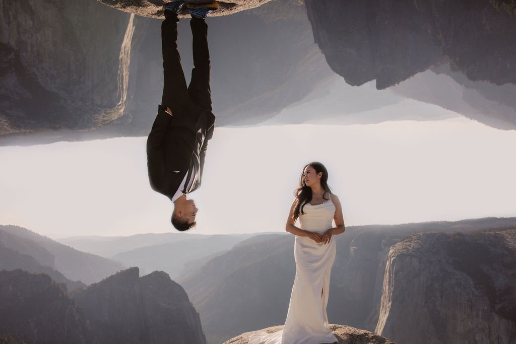 A couple dressed in wedding attire stands on a mountain ledge overlooking a vast rocky landscape with a prominent peak in the background. Best views in yosemite national park