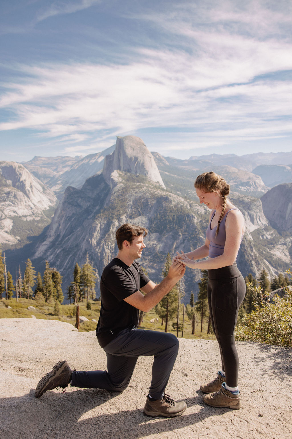 A person kneels and presents a ring to another person, who appears surprised. They are outdoors with mountains in the background. | How to Plan a Surprise Proposal at Yosemite National Park