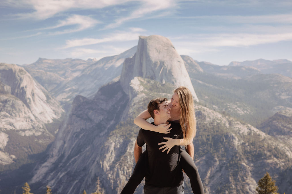 A person lifts another in an embrace with a scenic mountain landscape in the background. | How to Plan a Surprise Proposal at Yosemite National Park