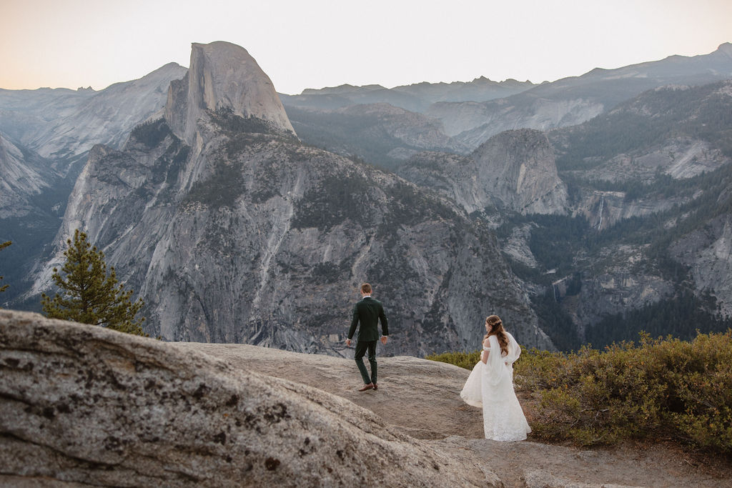 A couple exchanges vows with an officiant on a rocky overlook, with a mountain landscape in the background for a Yosemite elopement at Glacier Point and Mariposa Grove