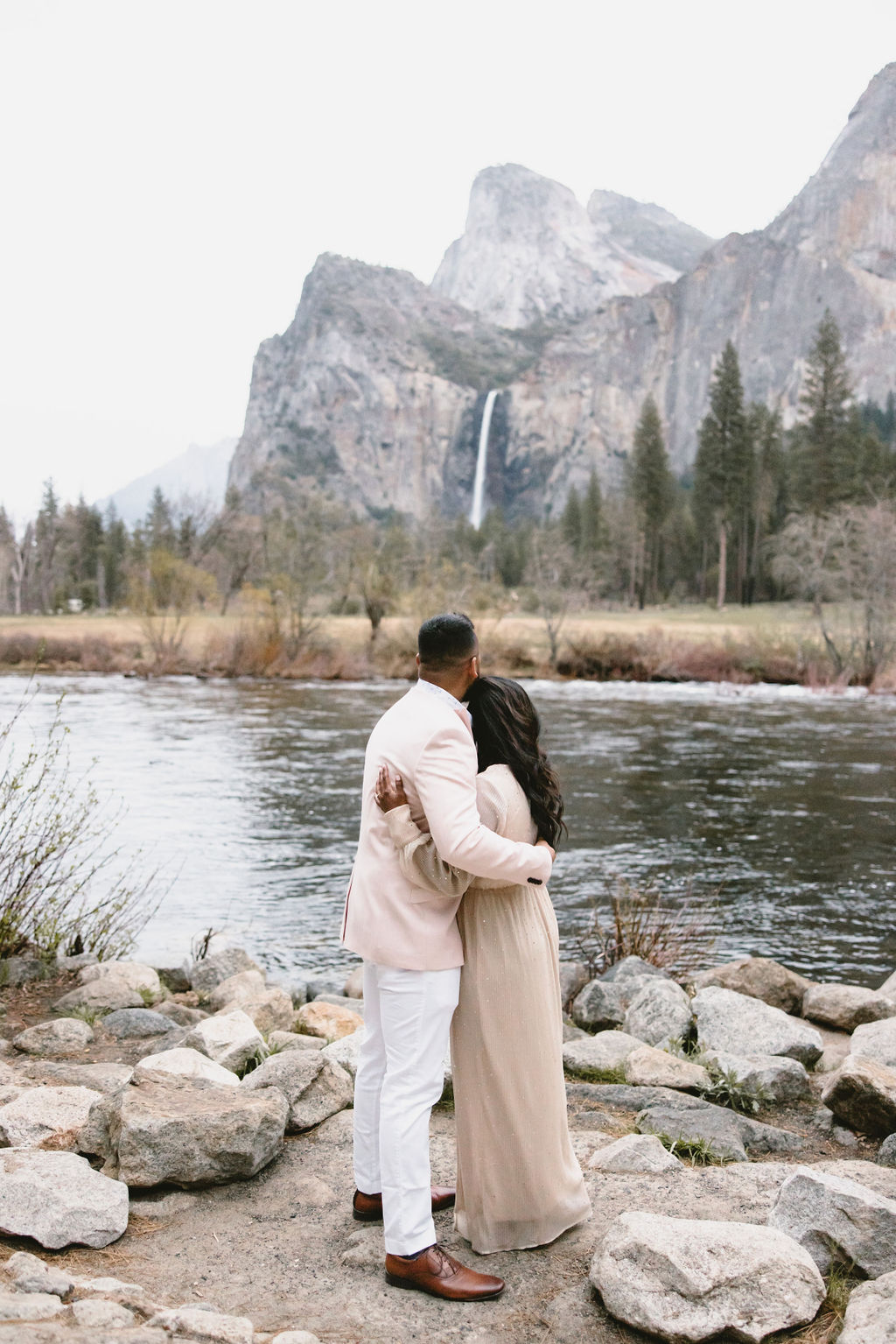 A couple embraces while facing a river and distant mountains with a waterfall.