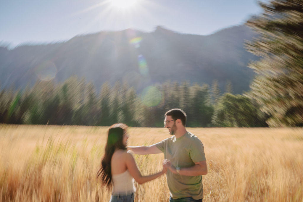 A couple smiling and embracing in front of a rocky river with tall mountains and trees in the background for their yosemite national park engagement photos