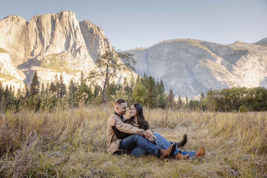 A couple holds hands and spins in a meadow with mountains and trees in the background at swinging bridge meadow for yosemite engaement photos