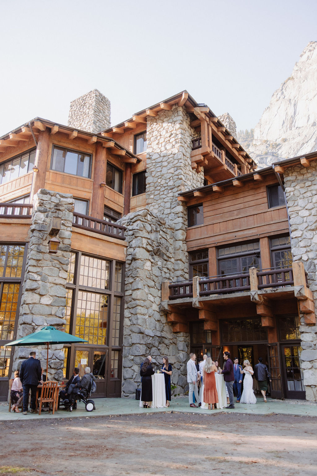 A group of people stand outside a large stone and wood building with balconies and large windows, on a clear day at Ahwahnee Hotel 