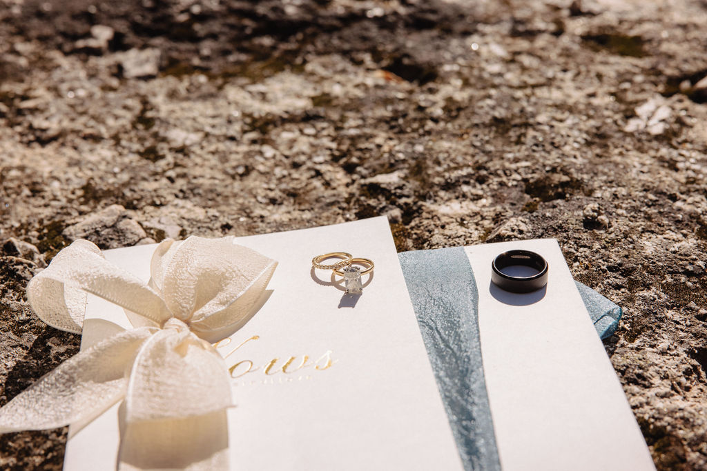 Floral wedding invitations and vow booklets with blue flowers, a wax seal, and a brass key on a textured surface.