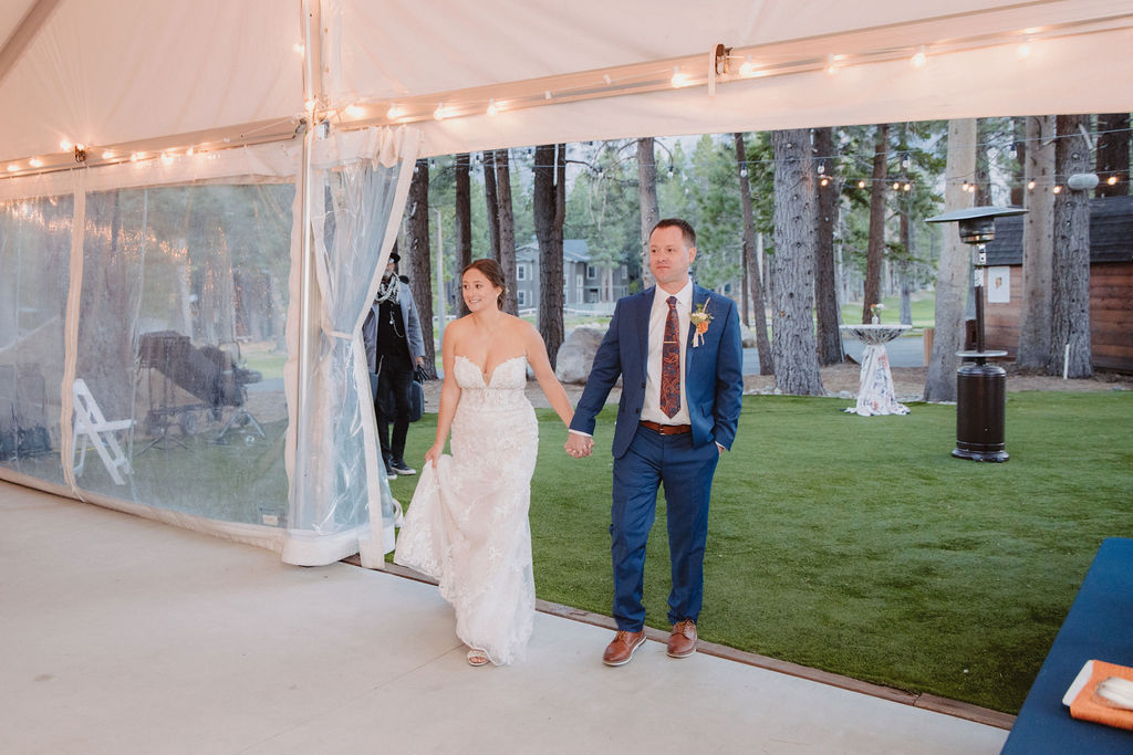 A couple in wedding attire kisses by a decorated table under string lights in a tent. at a wedding at sierra star golf course