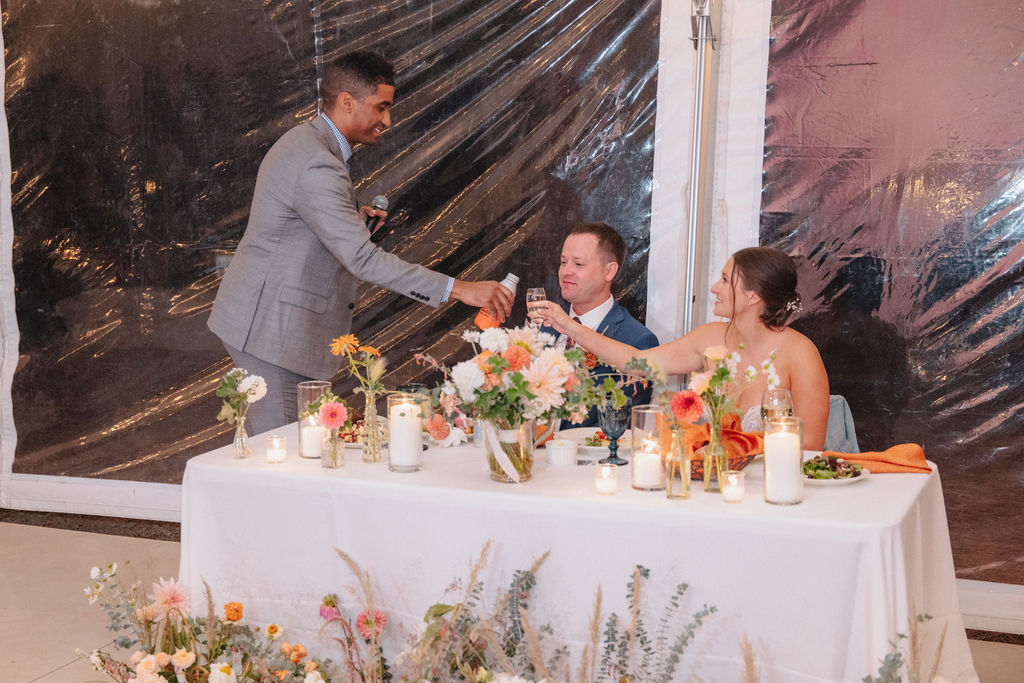 A person in a gray suit gives a toast to a seated couple at a decorated table with flowers and candles at a wedding at sierra star golf course