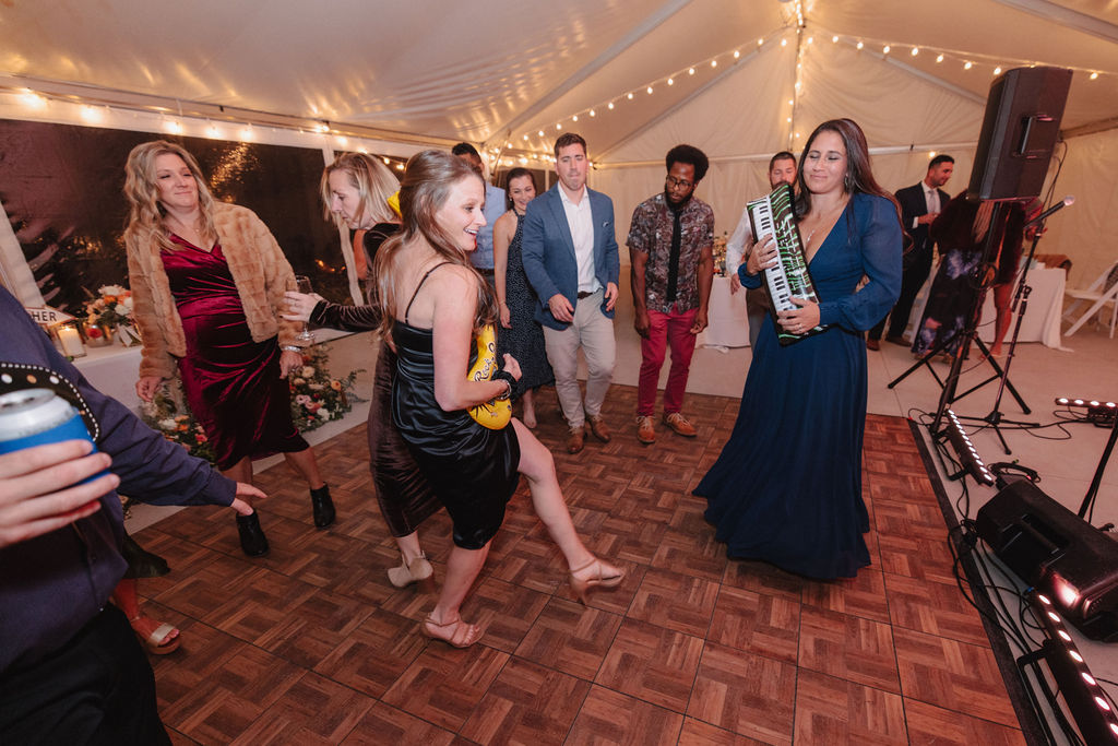 People dancing on a wooden floor under a tent with string lights, while a band plays in the background at a wedding at sierra star golf course