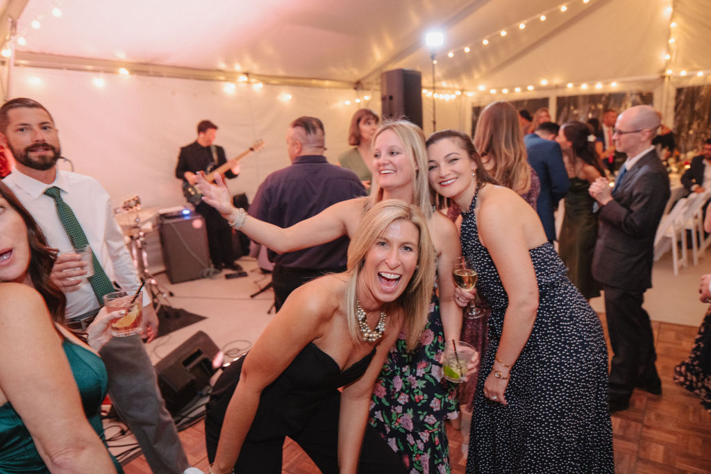 People dancing on a wooden floor under a tent with string lights, while a band plays in the background at a wedding at sierra star golf course