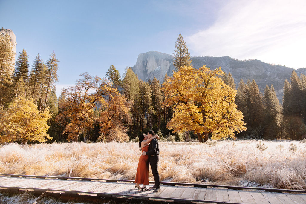 A couple stands in a scenic field with autumn trees and a mountain in the background for yosemite fall photos