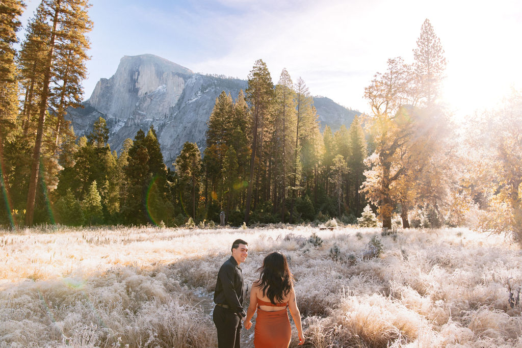 A couple stands in a scenic field with autumn trees and a mountain in the background for yosemite fall photos