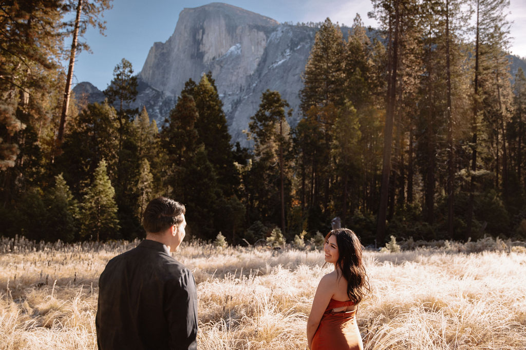 A couple stands in a scenic field with autumn trees and a mountain in the background for yosemite fall photos