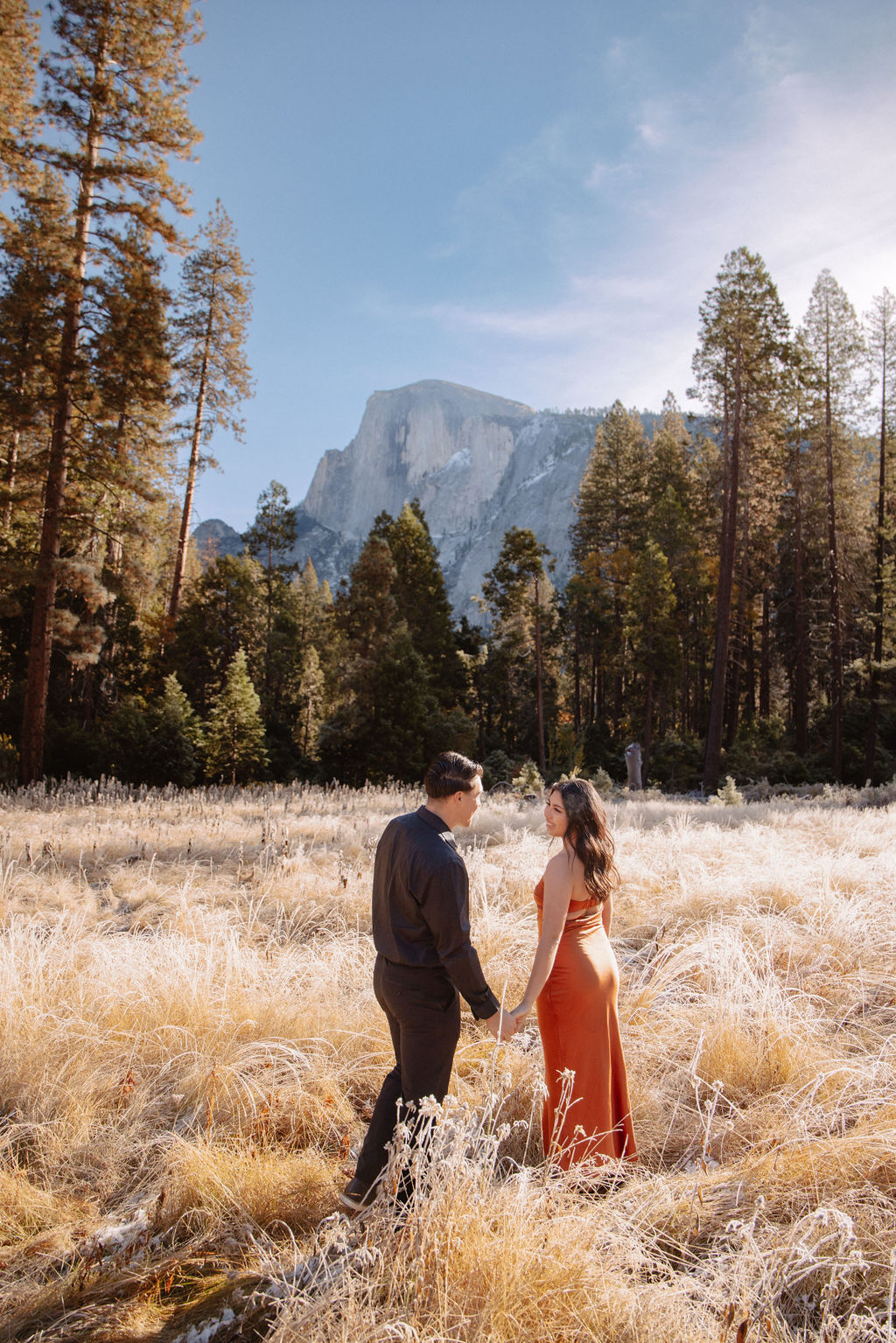 A couple stands in a scenic field with autumn trees and a mountain in the background for yosemite fall photos