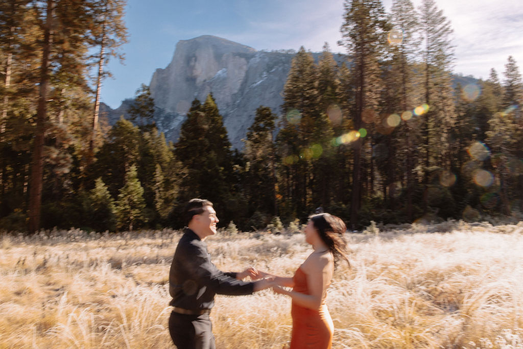 A couple stands in a scenic field with autumn trees and a mountain in the background for yosemite fall photos