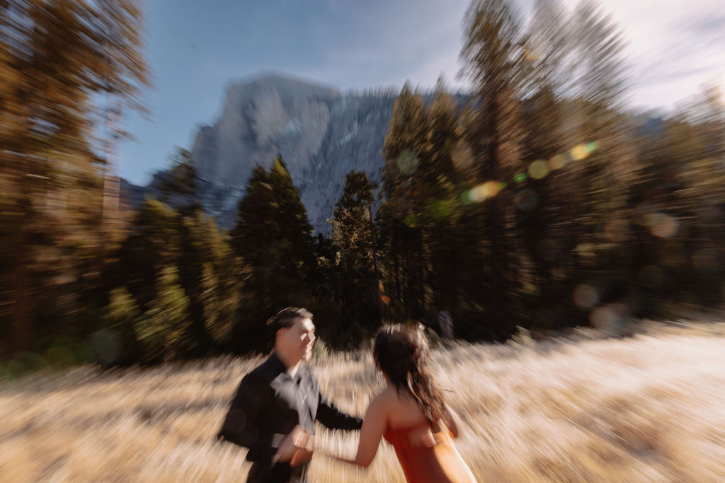 A couple stands in a scenic field with autumn trees and a mountain in the background for yosemite fall photos