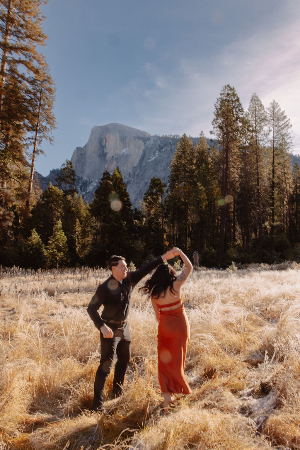 A couple stands in a scenic field with autumn trees and a mountain in the background for yosemite fall photos