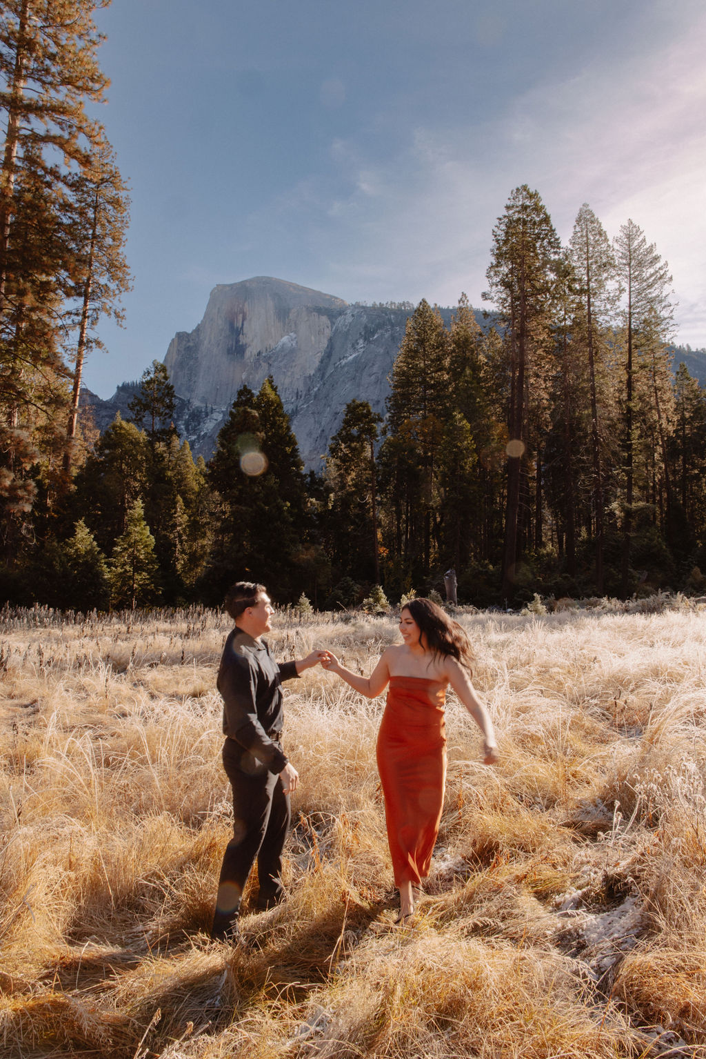 A couple stands in a scenic field with autumn trees and a mountain in the background for yosemite fall photos