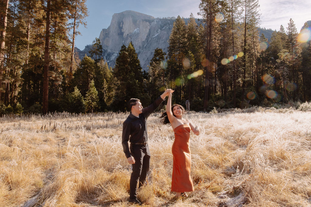 A couple stands in a scenic field with autumn trees and a mountain in the background for yosemite fall photos