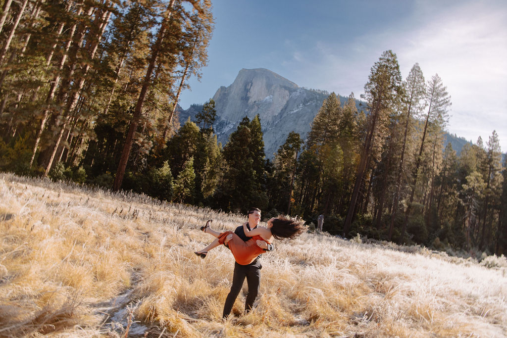 A couple stands in a scenic field with autumn trees and a mountain in the background for yosemite fall photos