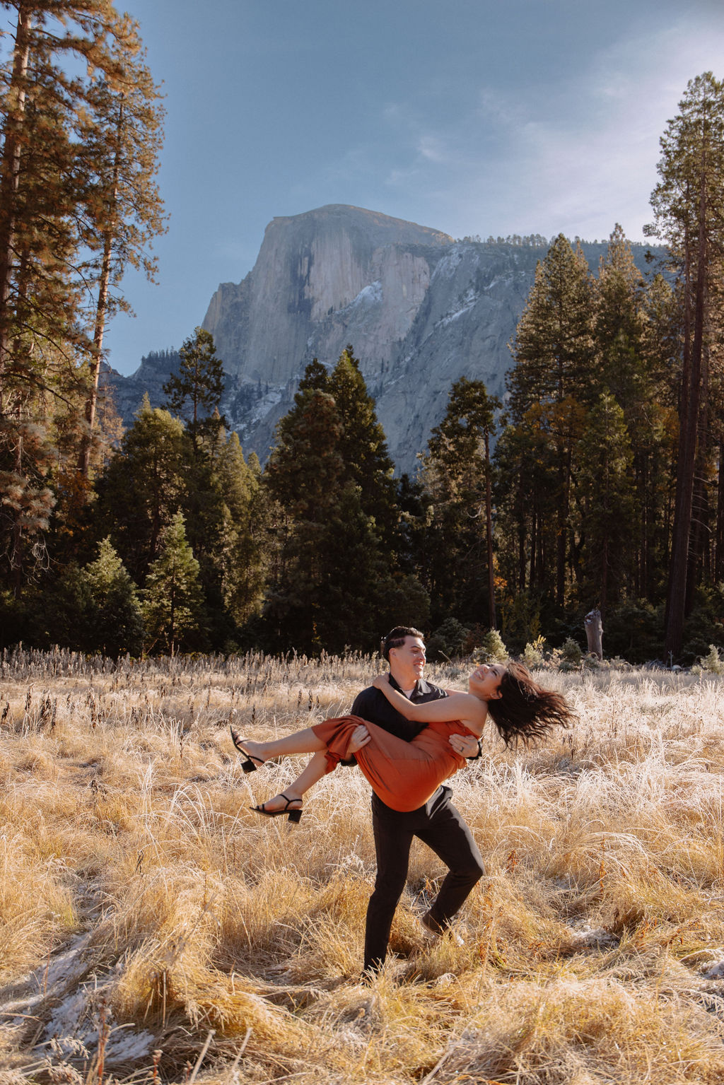 A couple stands in a scenic field with autumn trees and a mountain in the background for yosemite fall photos