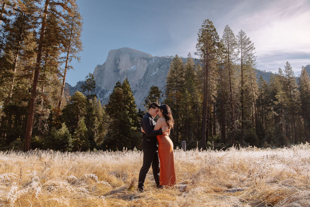 A couple stands in a scenic field with autumn trees and a mountain in the background for yosemite fall photos