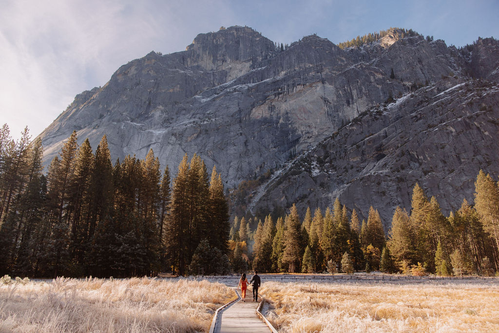 A couple stands in a scenic field with autumn trees and a mountain in the background for yosemite fall photos