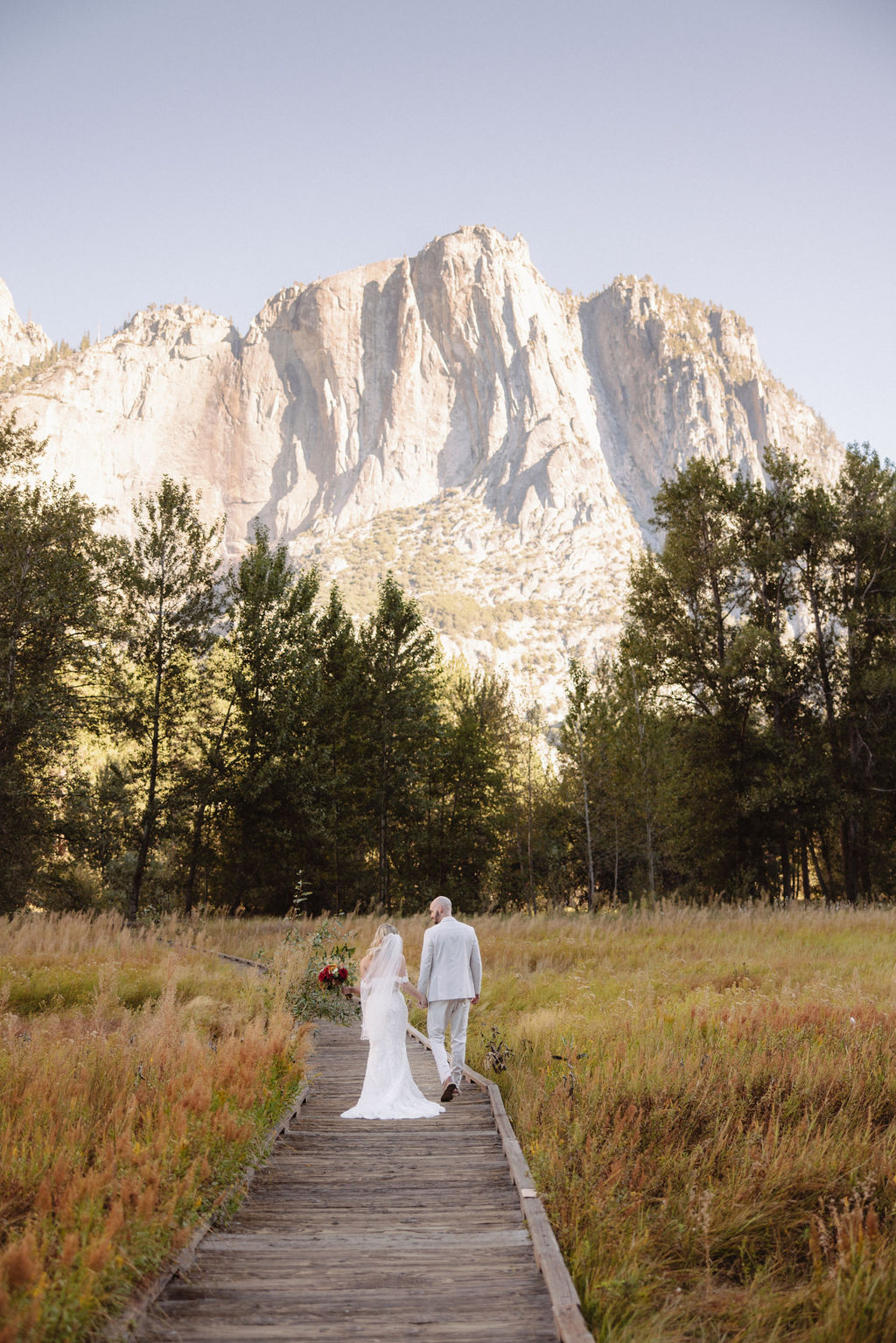 Bride and groom embracing on a rocky hilltop, with sunlight in the background and a mountain view for a sustainable wedding tips