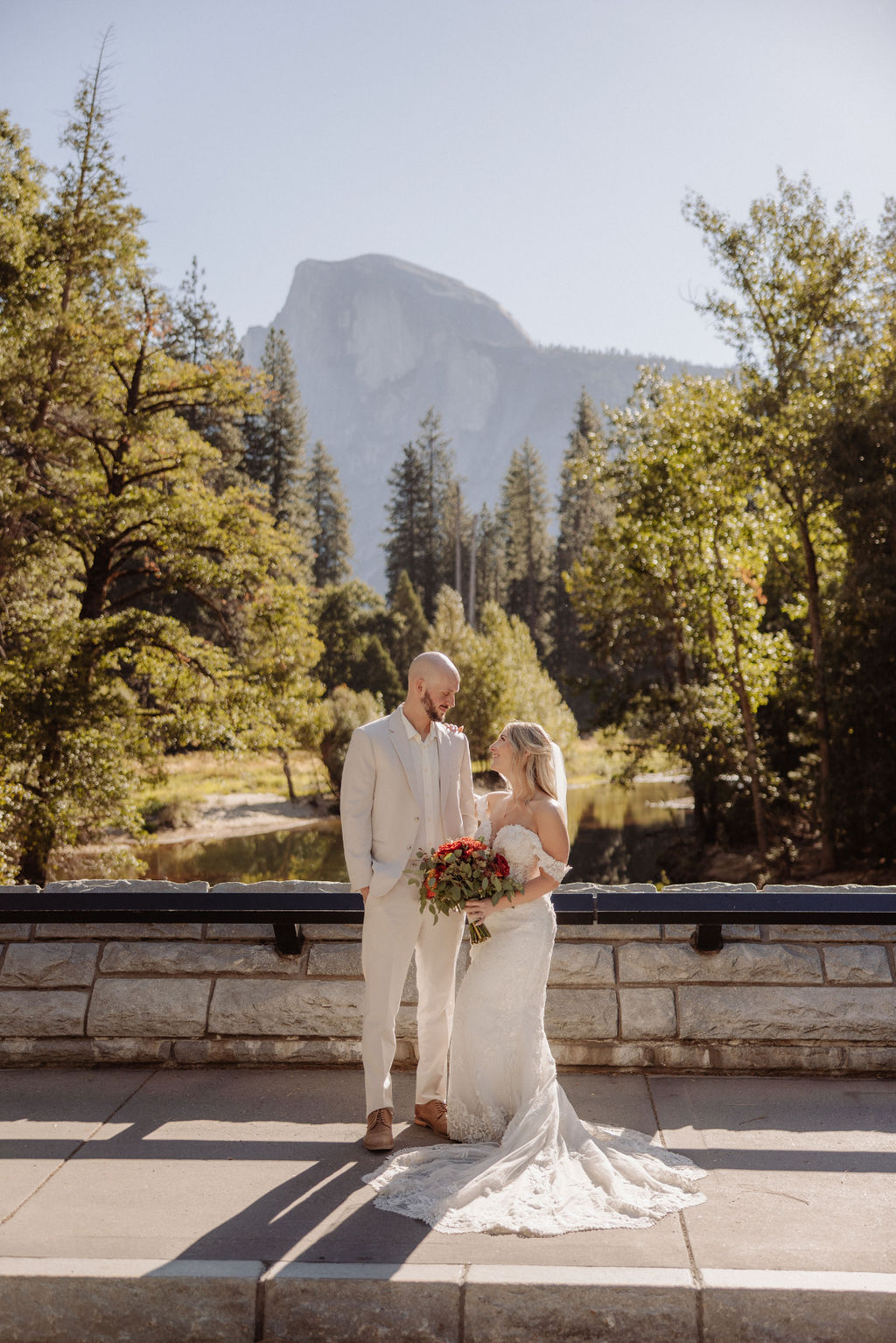 Bride and groom embracing on a rocky hilltop, with sunlight in the background and a mountain view for a sustainable wedding tips