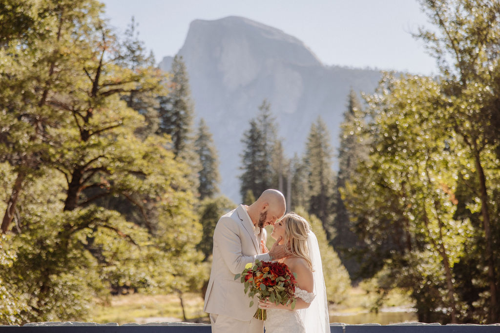 Bride and groom embracing on a rocky hilltop, with sunlight in the background and a mountain view for a sustainable wedding tips