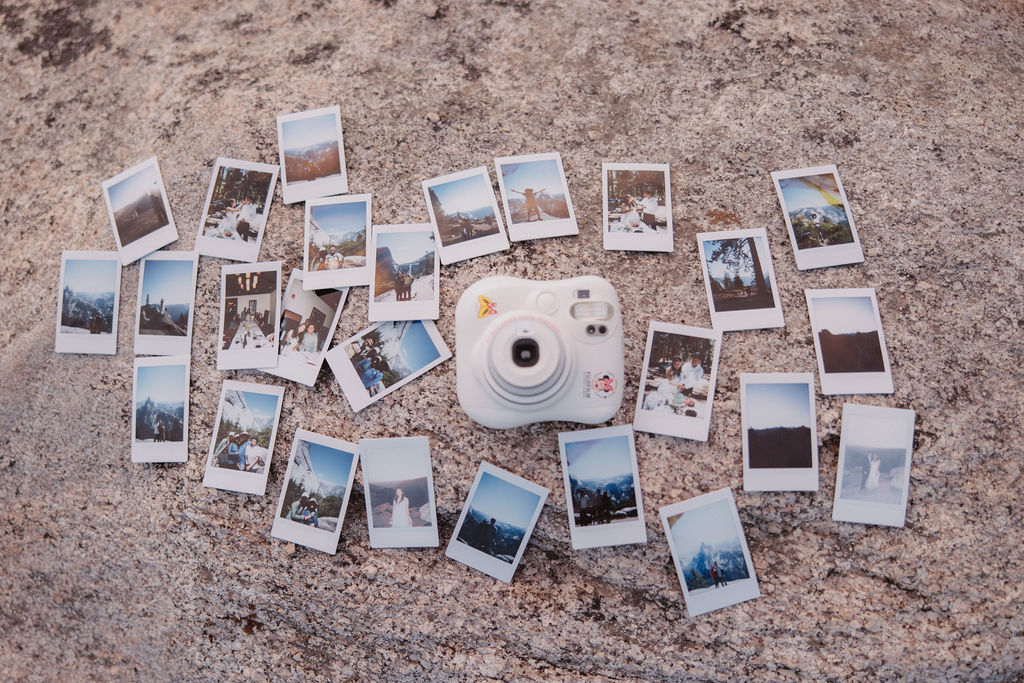 A white instant camera surrounded by various developed photo prints lies on a textured stone surface.