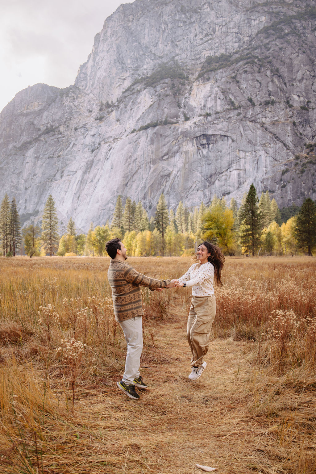 A couple stands in a sunlit field surrounded by trees, looking at each other affectionately. Sunlight creates a warm, golden glow taken by a yosemite proposal photographer