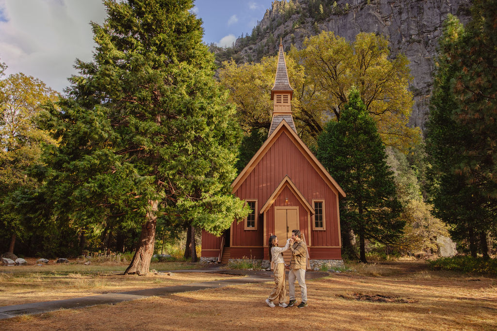 A couple stands in a sunlit field surrounded by trees, looking at each other affectionately. Sunlight creates a warm, golden glow taken by a yosemite proposal photographer