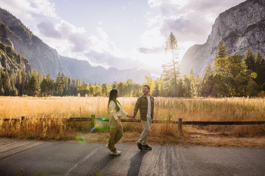 A couple stands in a sunlit field surrounded by trees, looking at each other affectionately. Sunlight creates a warm, golden glow taken by a yosemite proposal photographer