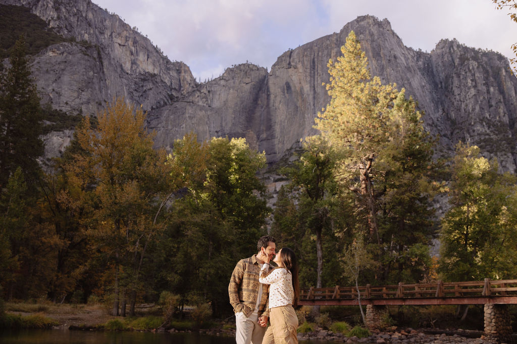 A couple stands in a sunlit field surrounded by trees, looking at each other affectionately. Sunlight creates a warm, golden glow taken by a yosemite proposal photographer