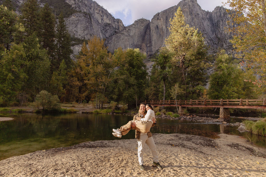 A couple stands in a sunlit field surrounded by trees, looking at each other affectionately. Sunlight creates a warm, golden glow taken by a yosemite proposal photographer